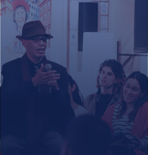 A man speaking at an in-person event with audience members listening along.