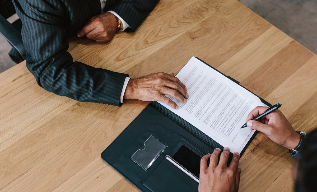 Overview shot of one person offering the other a contract on a wooden table.