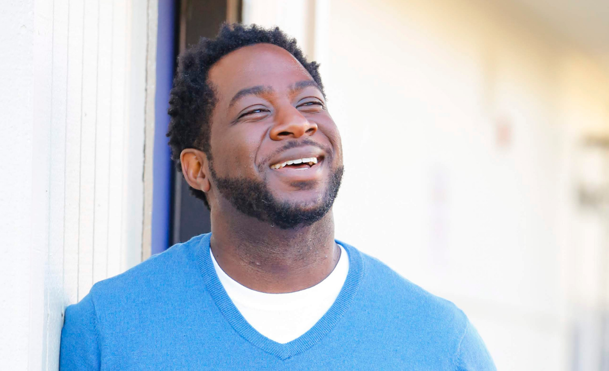 A man wearing a blue shirt (Corey Ponder) smiles and looks past the camera.